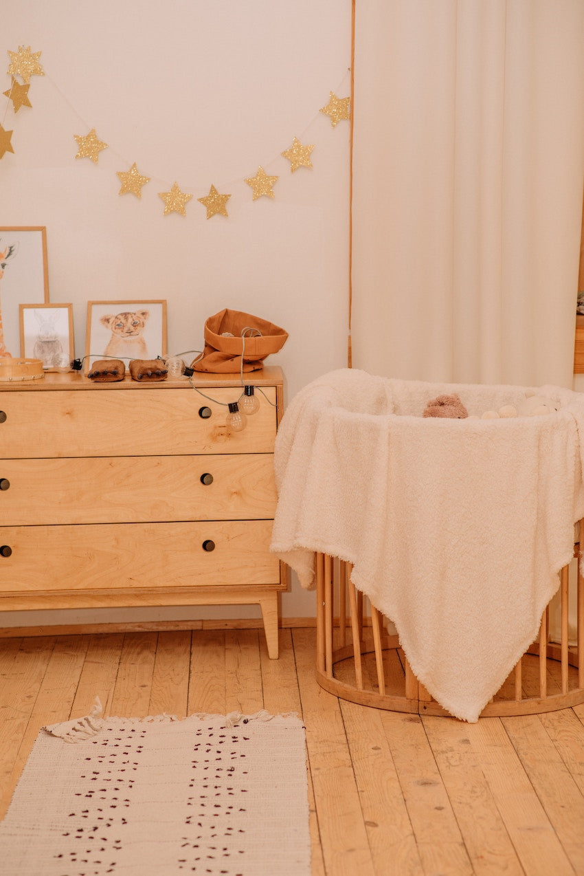 image d'une chambre pour bébé avec une commode et un petit landau circulaire, le tout en bois clair et avec une guirlande d'étoiles accrochée au mur. Image